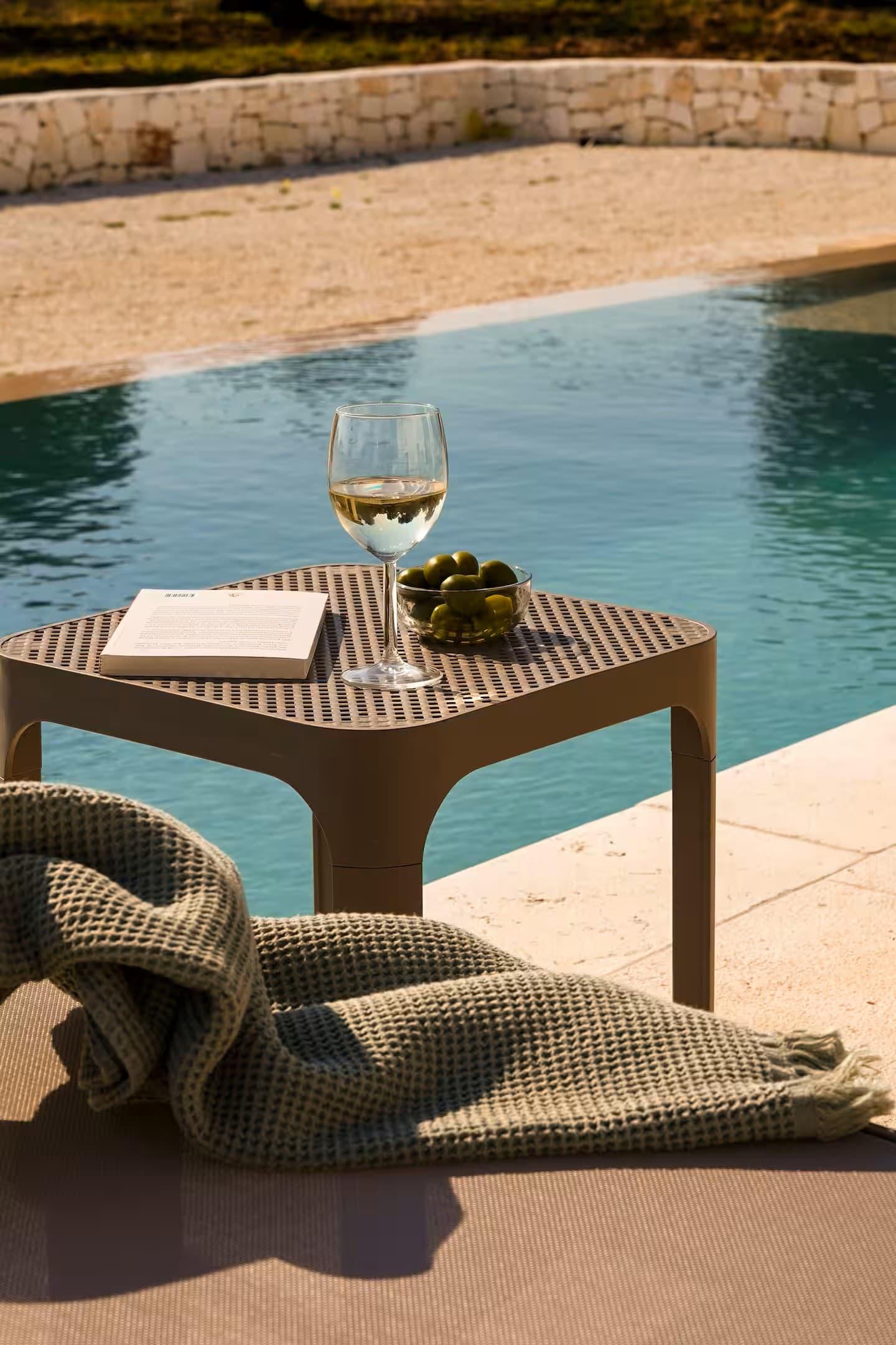 Poolside table with a glass of wine, a bowl of olives, and a book